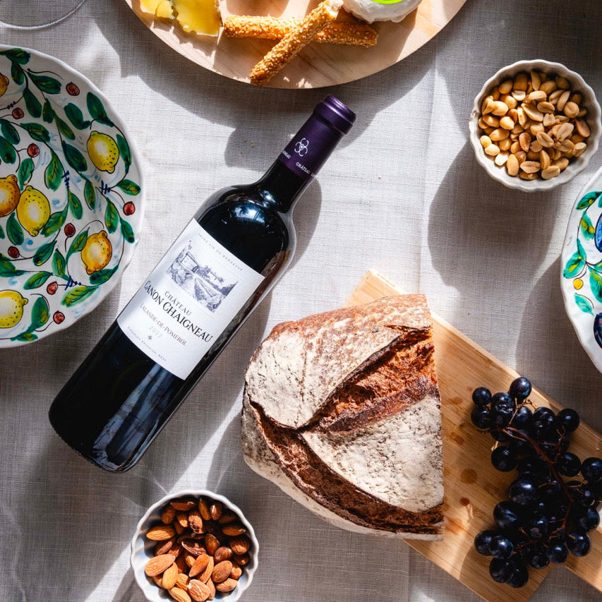 Assorted cheeses, crackers, grapes, and a bottle of wine on a table with a decorative tablecloth.
